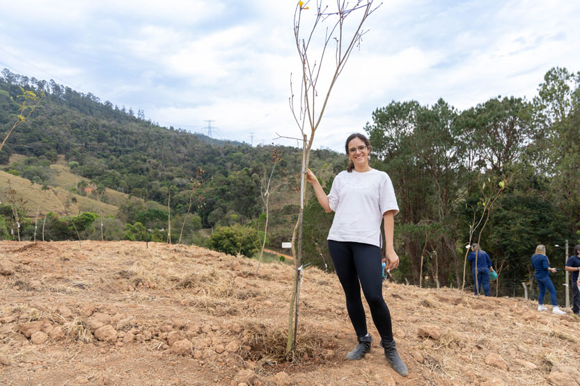 Fotografia da deputada estadual Marina Helou ao lado de uma muda de árvore na área de reflorestamento da Unidade de Lazer AFPESP Serra Negra.